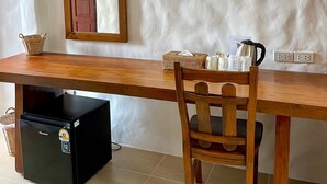 A room with a wooden table, a chair, a small black refrigerator, a wicker basket, a wooden cabinet, and a wall-mounted mirror. - Gee Resort (Koh Tao)