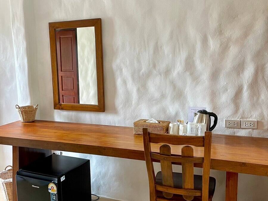 Una habitación con una mesa de madera, una silla, un refrigerador negro pequeño, una cesta de mimbre, un armario de madera y un espejo adosado a la pared.