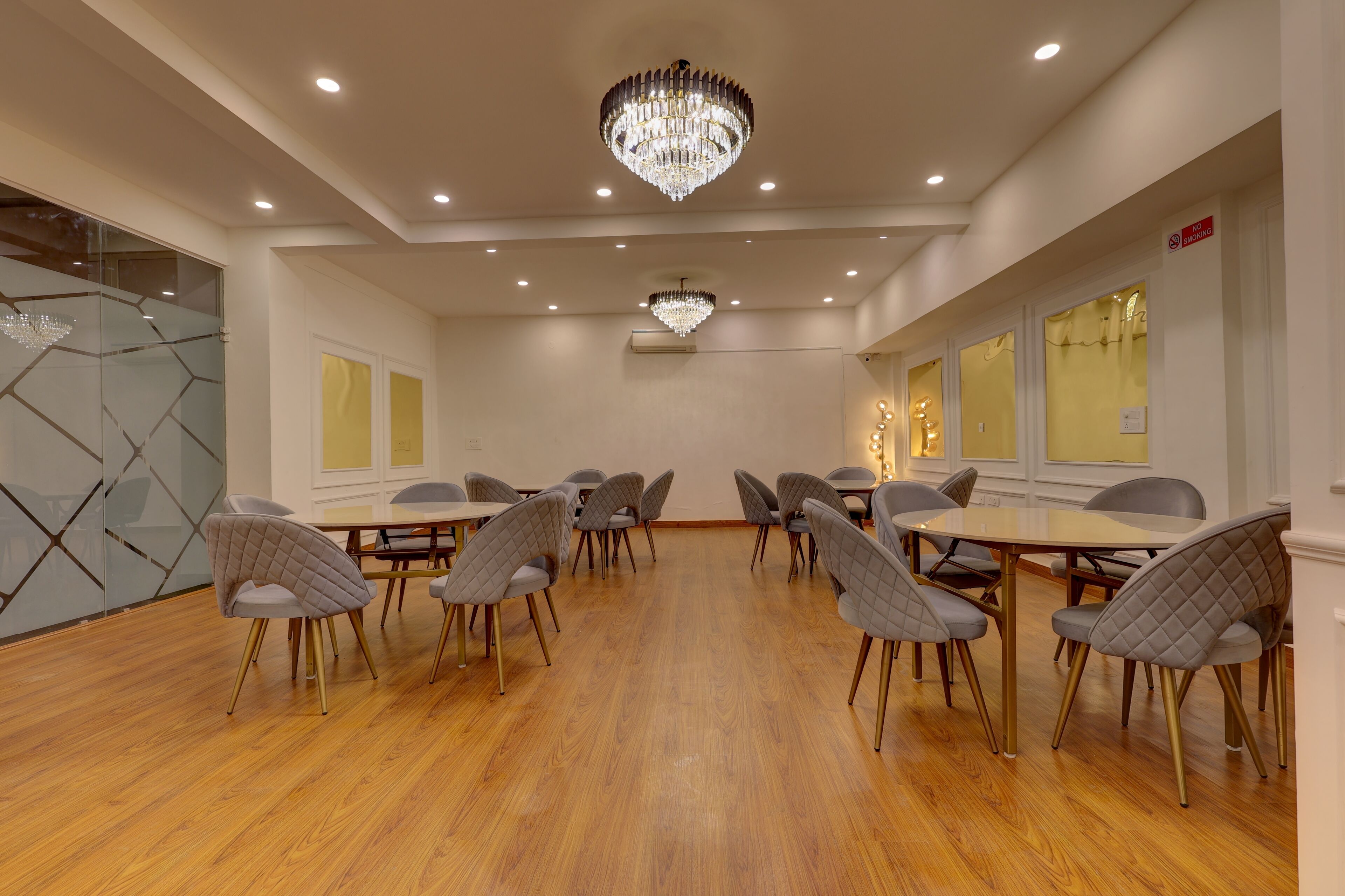 Un salón de conferencias con suelo de madera, sillas tapizadas en gris, una lámpara de araña grande y una pared divisoria de vidrio.