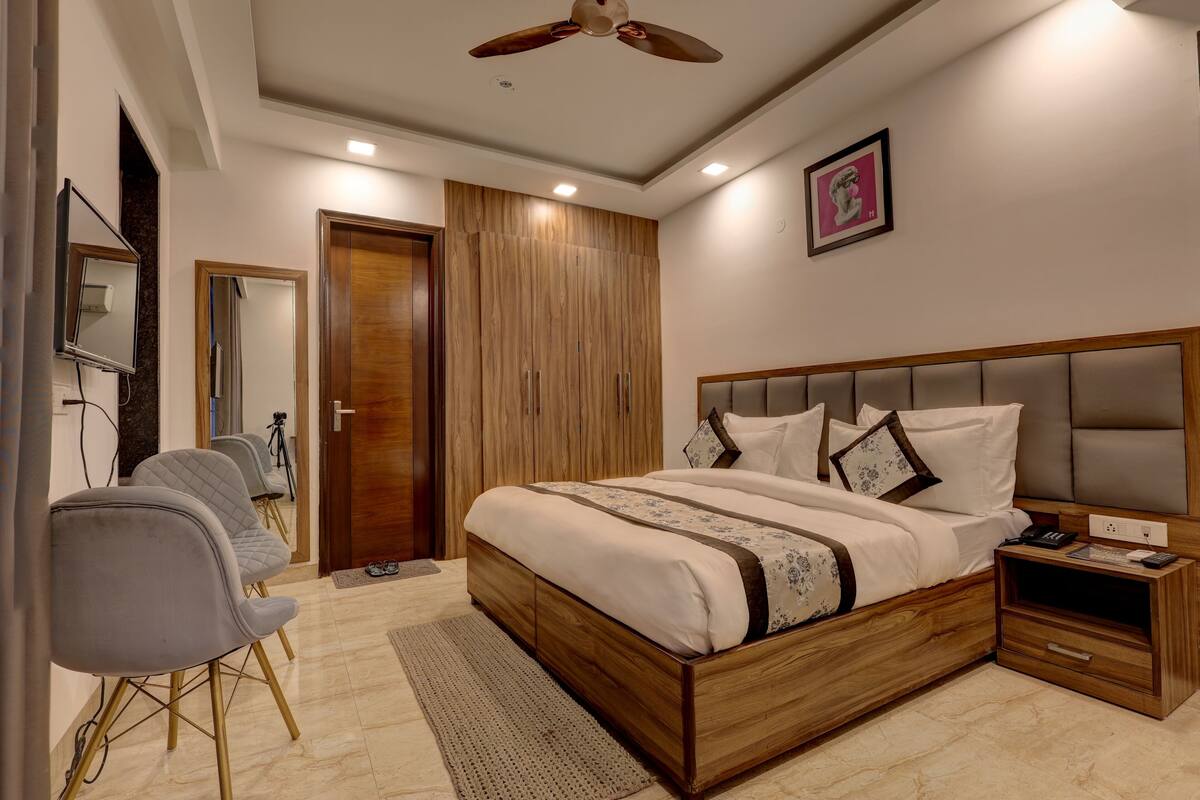 A modern bedroom with a large bed, a ceiling fan, a wooden wardrobe, and a small bedside table.