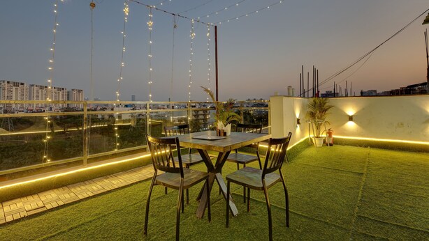 Un área de comedor al aire libre con mesa y sillas, luces colgantes y vistas de la ciudad.