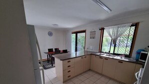 A kitchen with a central island, a dining area with chairs, and a refrigerator. - Welcome to "Seascapes" (Gympie)