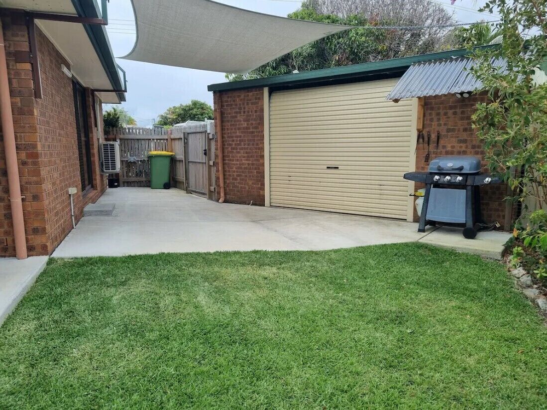 A residential backyard with a garage, a barbecue grill, and a covered patio area.