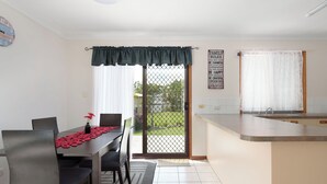A dining area with a table, chairs, and a view through a sliding glass door. - Welcome to "Seascapes" (Gympie)