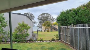 A covered patio area with a view of a backyard, a wooden fence, and a building in the background. - Welcome to "Seascapes" (Gympie)