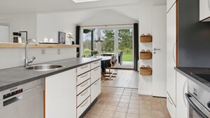Eine moderne Küche mit eingebautem Geschirrspüler, einem großen Fenster und einem Essbereich mit Tisch und Stühlen.