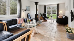 Ein modernes Wohnzimmer mit einem Glastisch, Ledersofas, einem Kamin und großen Fenstern mit Blick ins Freie.