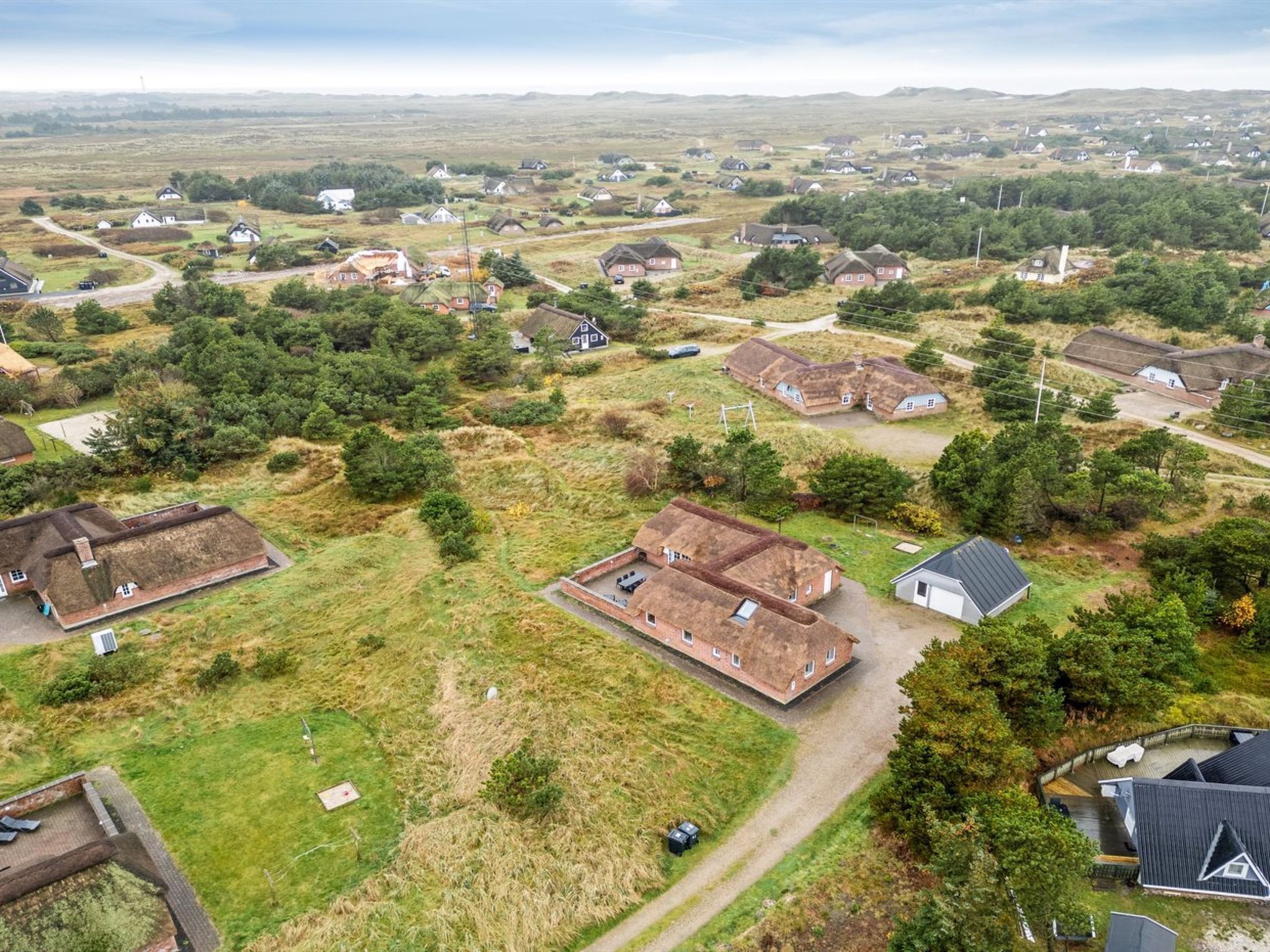 An aerial view of a rural village with traditional houses, a central building with a large roof, and surrounding greenery.