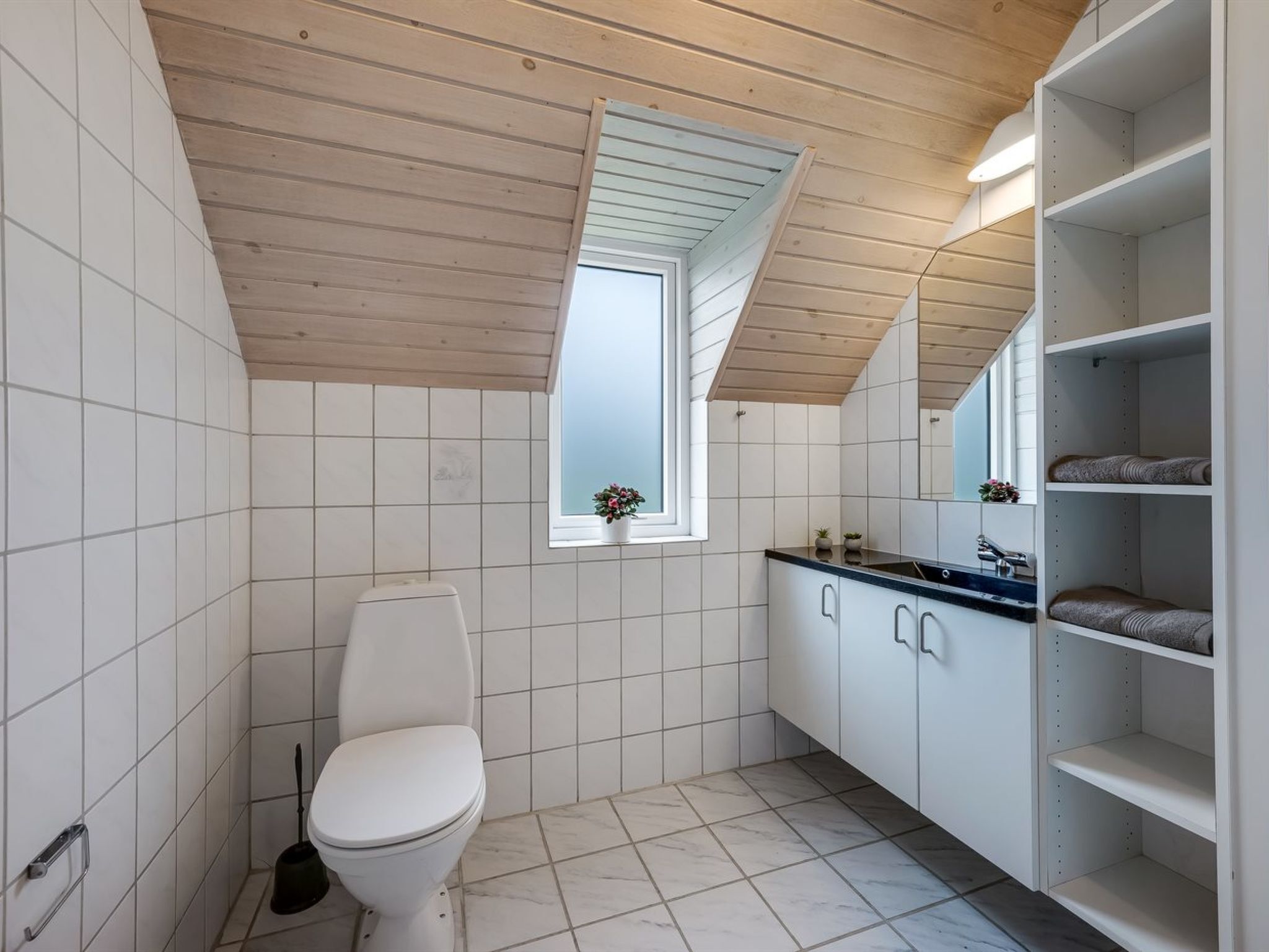 A modern bathroom with a white toilet, a small window, and a mirror above the sink.