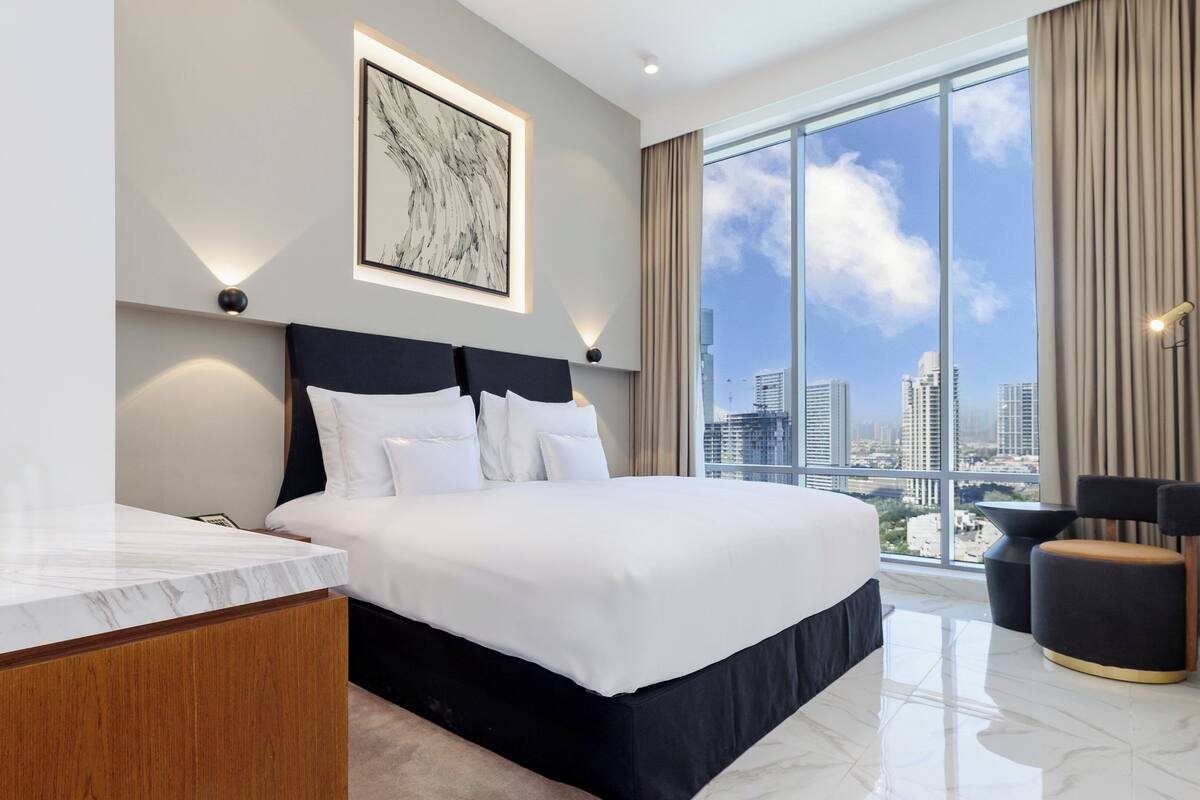 A modern hotel room with a large bed, a desk, and a view of the city skyline.