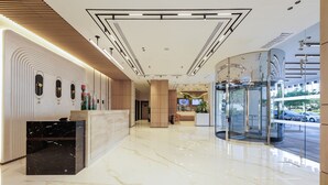 A modern hotel lobby with a marble floor, a reception desk, a glass elevator, and a seating area with a TV screen. - Holiday Inn Dubai Jumeirah Village Circle by IHG (Dubai)