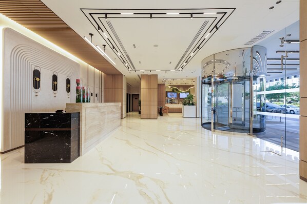 A modern hotel lobby with a marble floor, a reception desk, a glass elevator, and a seating area with a TV screen. - Holiday Inn Dubai Jumeirah Village Circle by IHG (Dubai)