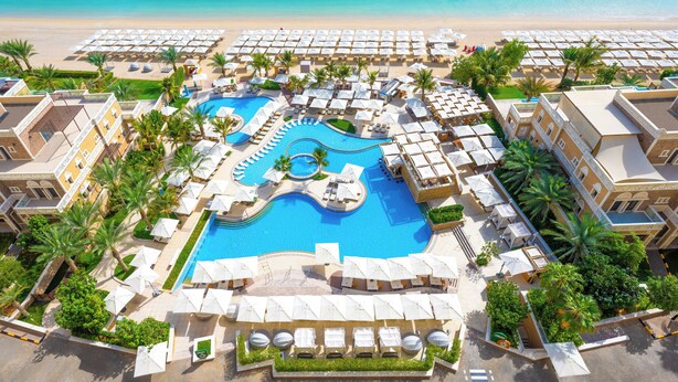A resort with a central swimming pool, multiple sun loungers, and a beach area. - Holiday Inn Dubai Jumeirah Village Circle by IHG (Dubai)
