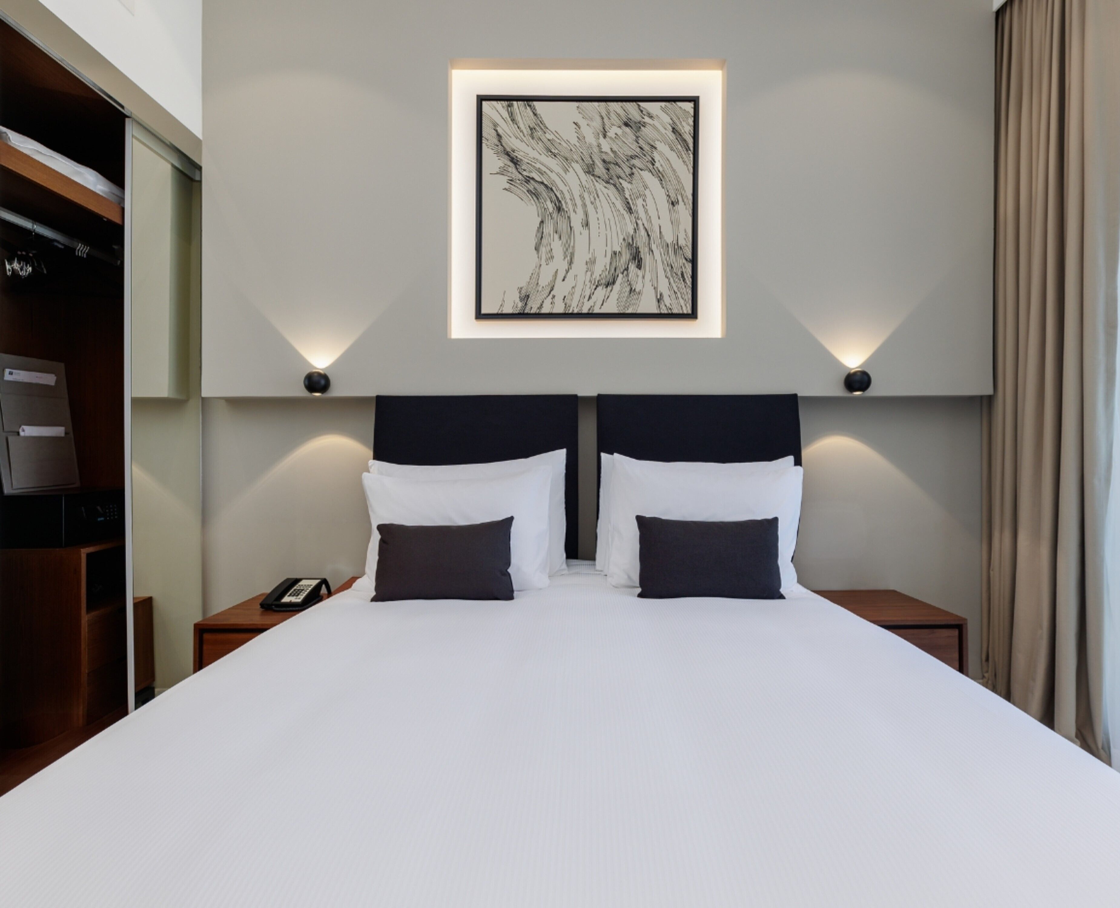 Habitación de hotel con una cama grande, dos mesitas de noche, un teléfono y una obra de arte enmarcada en la pared.