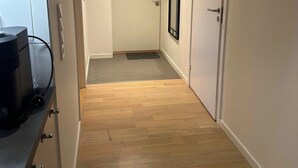Een hal met houten vloer, een witte deur aan het einde en een spiegel met zwart frame aan de muur.