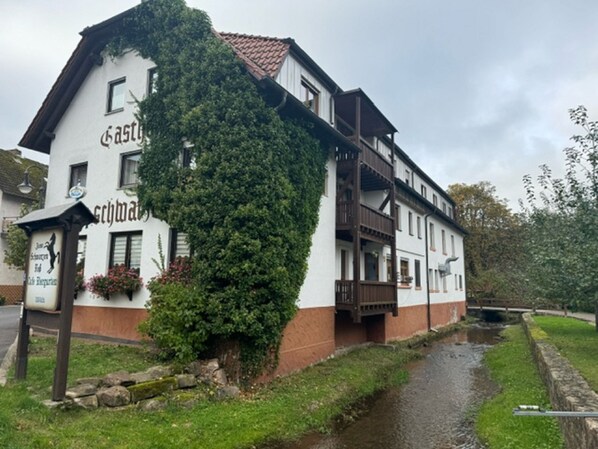 A two-story building with a white facade and brown trim, featuring a balcony and a sign that reads "Castles." - Gasthof Zum schwarzen Roß (Zeitlofs)