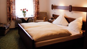 A hotel room with a double bed, a chair, a small table with a vase of flowers, and a window with curtains. - Gasthof Zum schwarzen Roß (Zeitlofs)