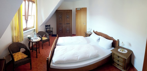 A bedroom with a large bed, a wooden nightstand, a chair, a small table, and a wardrobe. - Gasthof Zum schwarzen Roß (Zeitlofs)