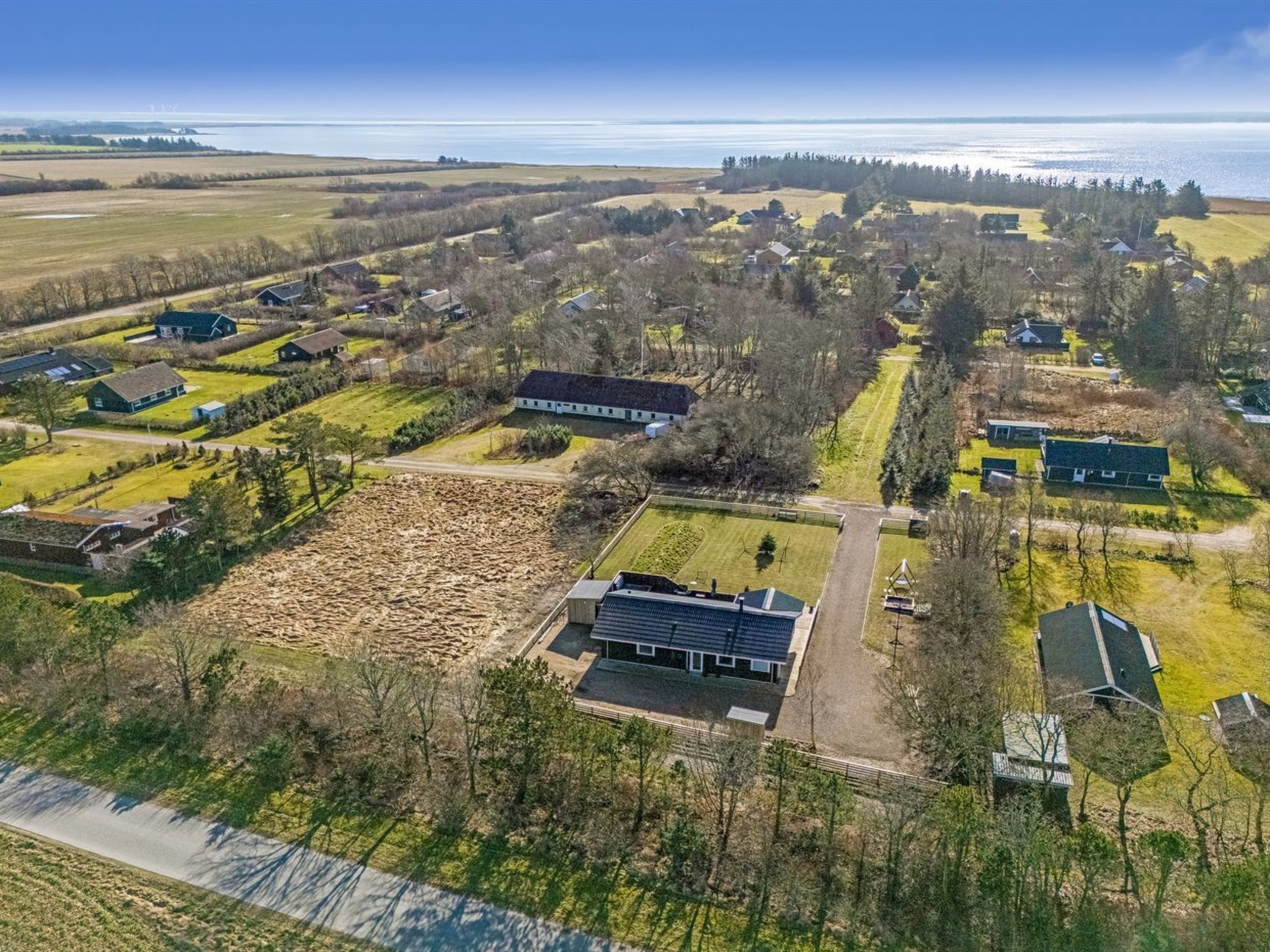 Vue aérienne d’une zone rurale avec des maisons, des champs ouverts et une grande étendue d’eau en arrière-plan.