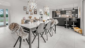 A modern kitchen with a central island, a dining area with a white table and chairs, and a large window with a view of greenery. - "Elisaveta" - 400m to the fjord by Interhome (Vemb)
