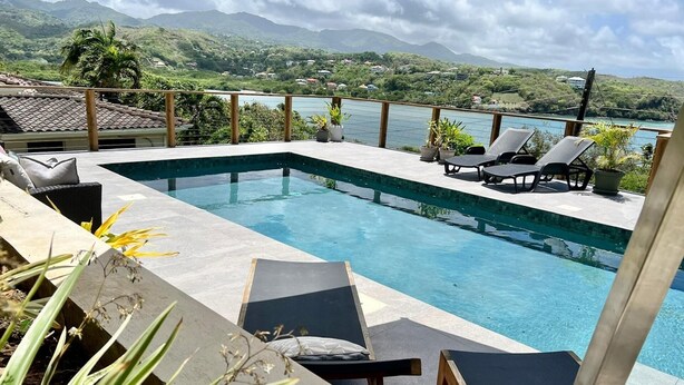 Piscina retangular com borda ladrilhada, rodeada por espreguiçadeiras e plantas em vasos.