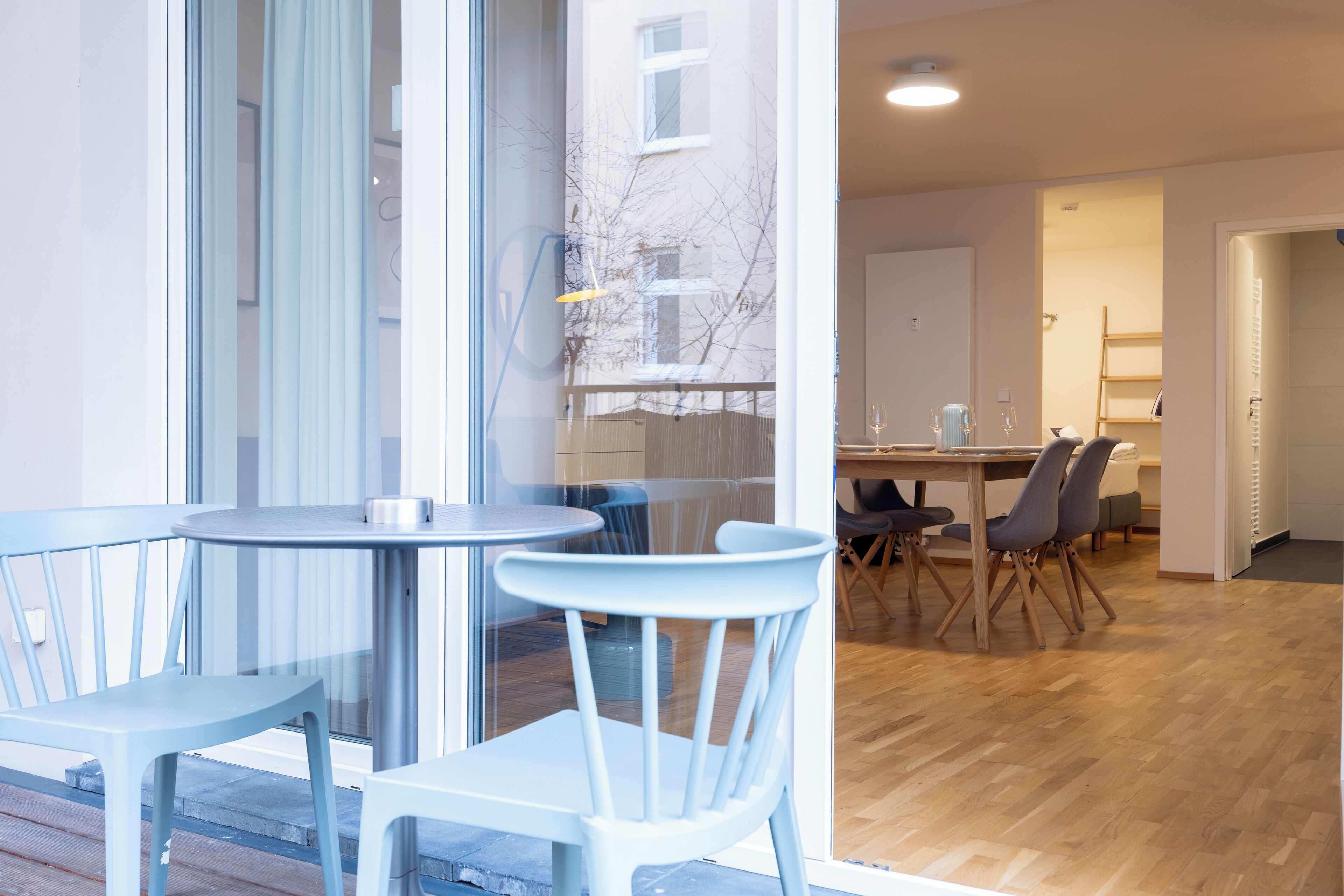 Un interior moderno con zona de comedor que incluye una mesa redonda y sillas, una cocina al fondo y vistas a través de un ventanal.