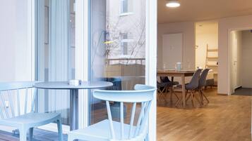 Un interior moderno con zona de comedor que incluye una mesa redonda y sillas, una cocina al fondo y vistas a través de un ventanal.