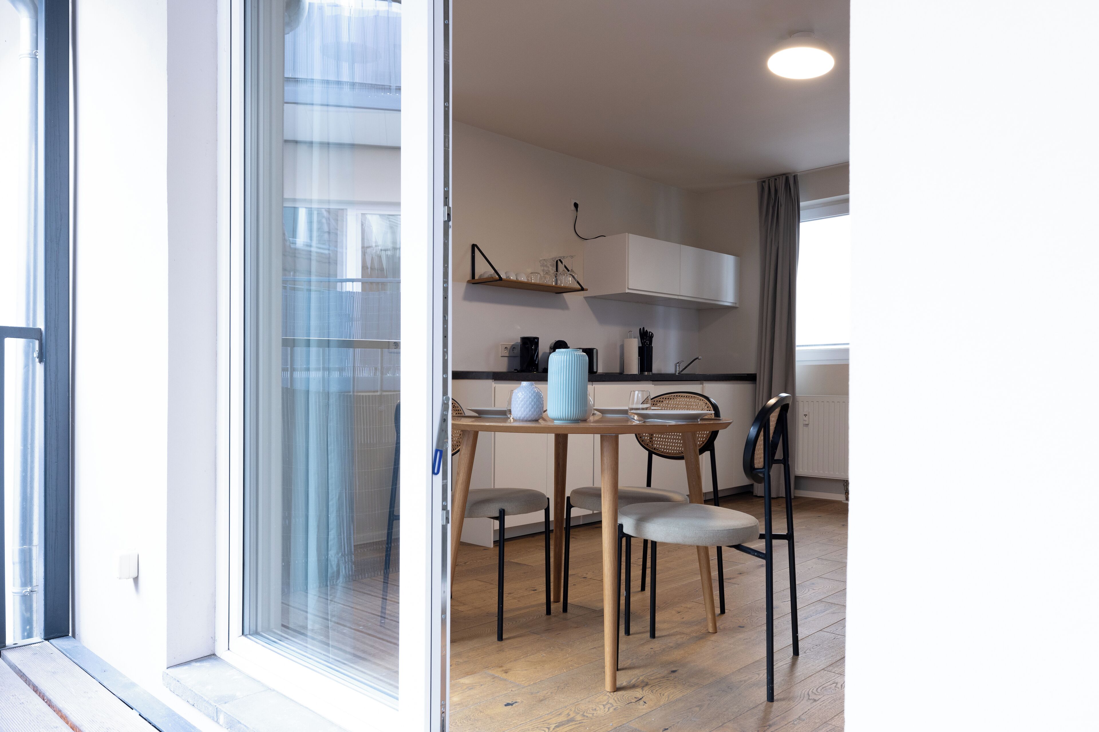 A modern kitchen with white cabinets, a wooden dining table, and a glass door leading to a balcony.