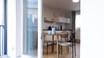 A modern kitchen with white cabinets, a wooden dining table, and a glass door leading to a balcony.