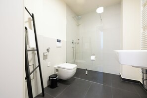 Une salle de bain moderne avec une douche à parois de verre, un lavabo blanc et une poubelle noire.
