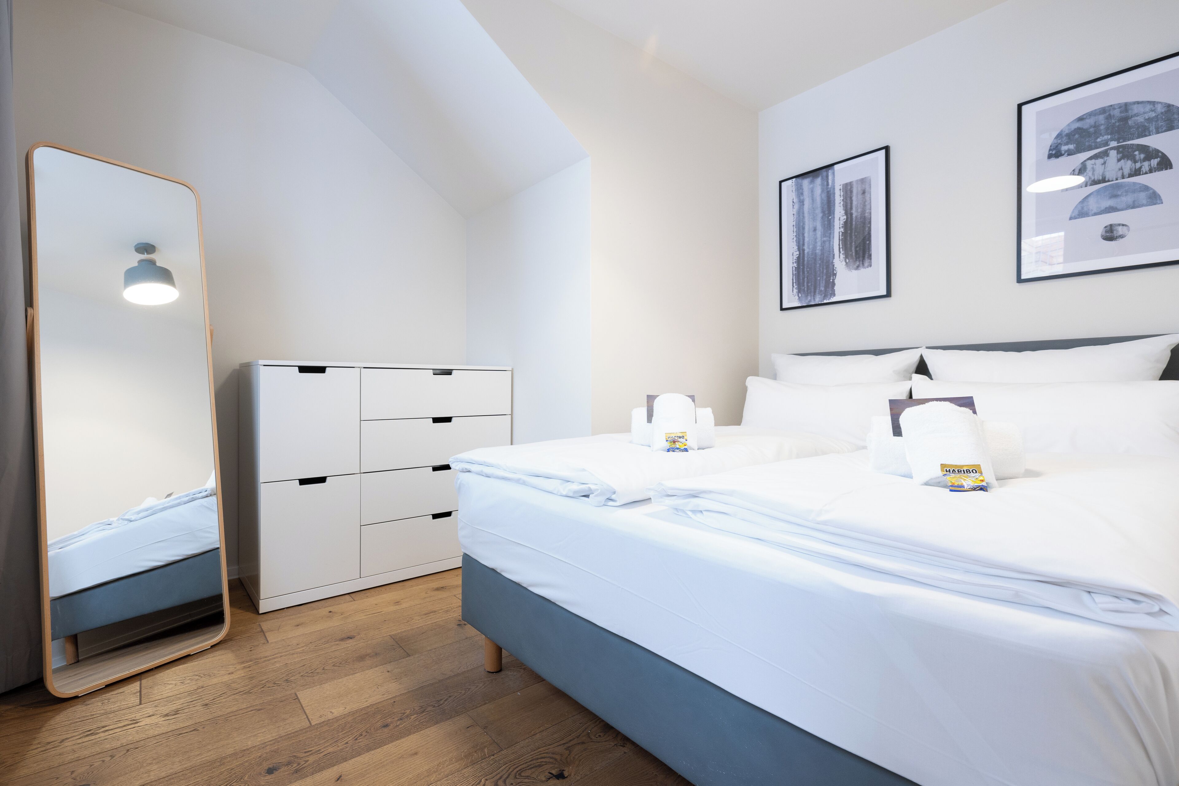 Een moderne slaapkamer met een bed, een kledingkast, een spiegel en twee ingelijste foto’s aan de muur.