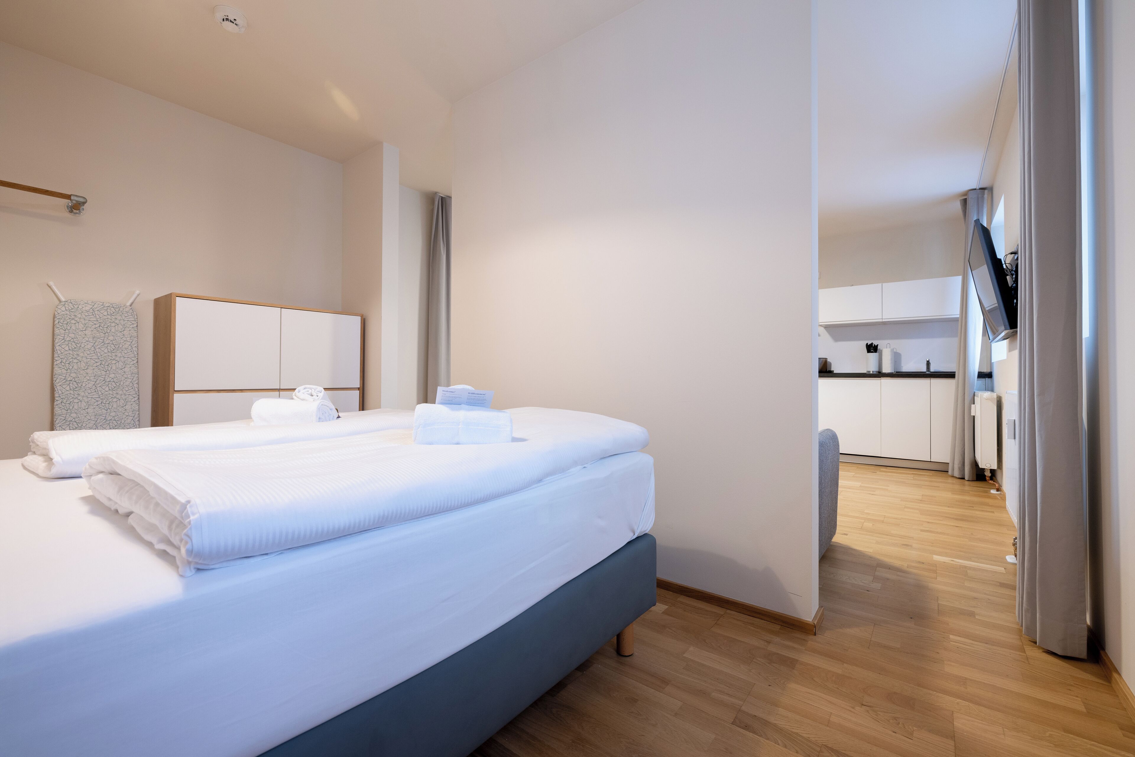 Una habitación de hotel moderna con una cama grande, un escritorio pequeño y una kitchenette al fondo.