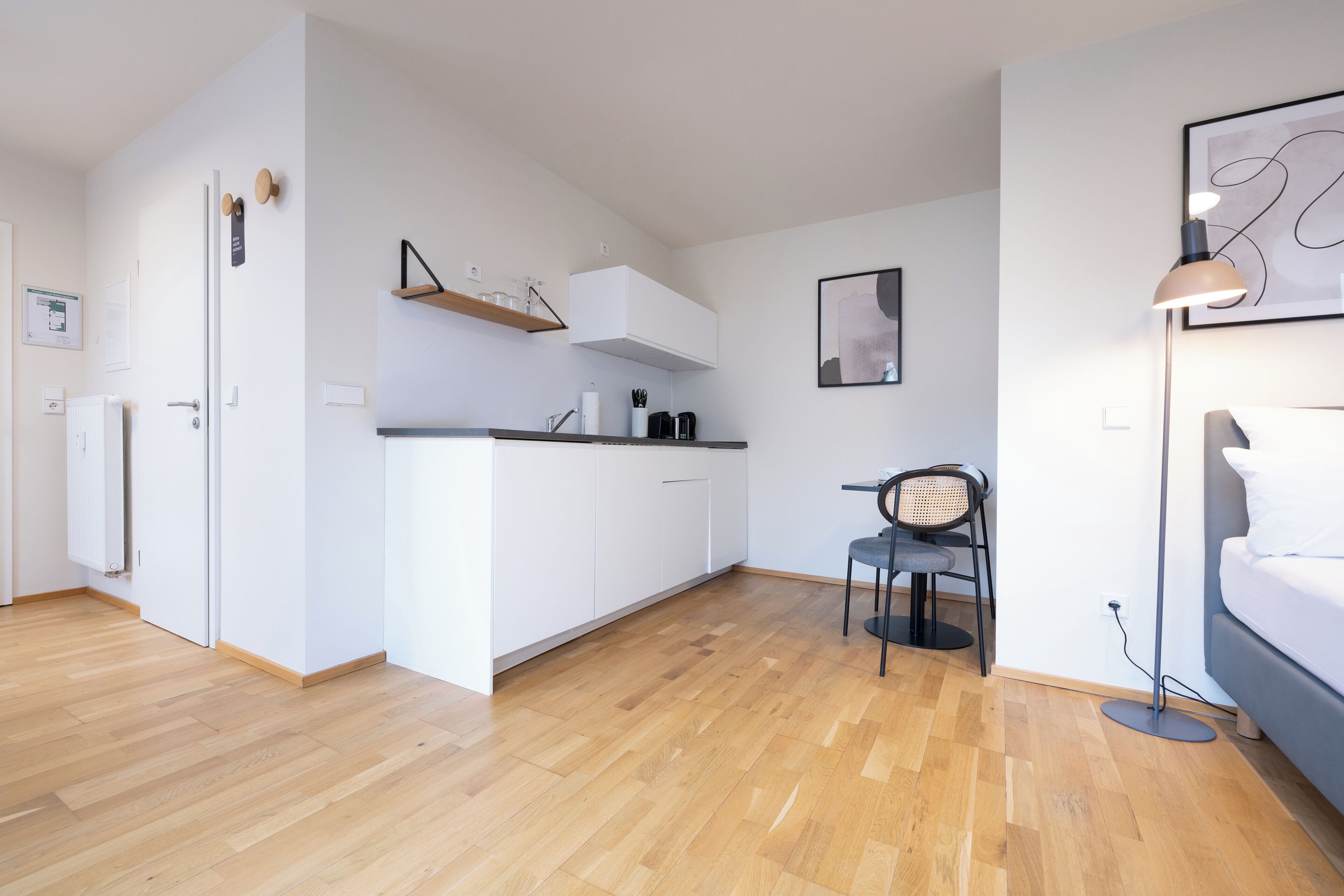 Una cocina moderna con armarios blancos, suelo de madera y un comedor con una silla y una mesa.