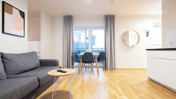 A modern living room with a grey sofa, a small round table, and a dining area with chairs.