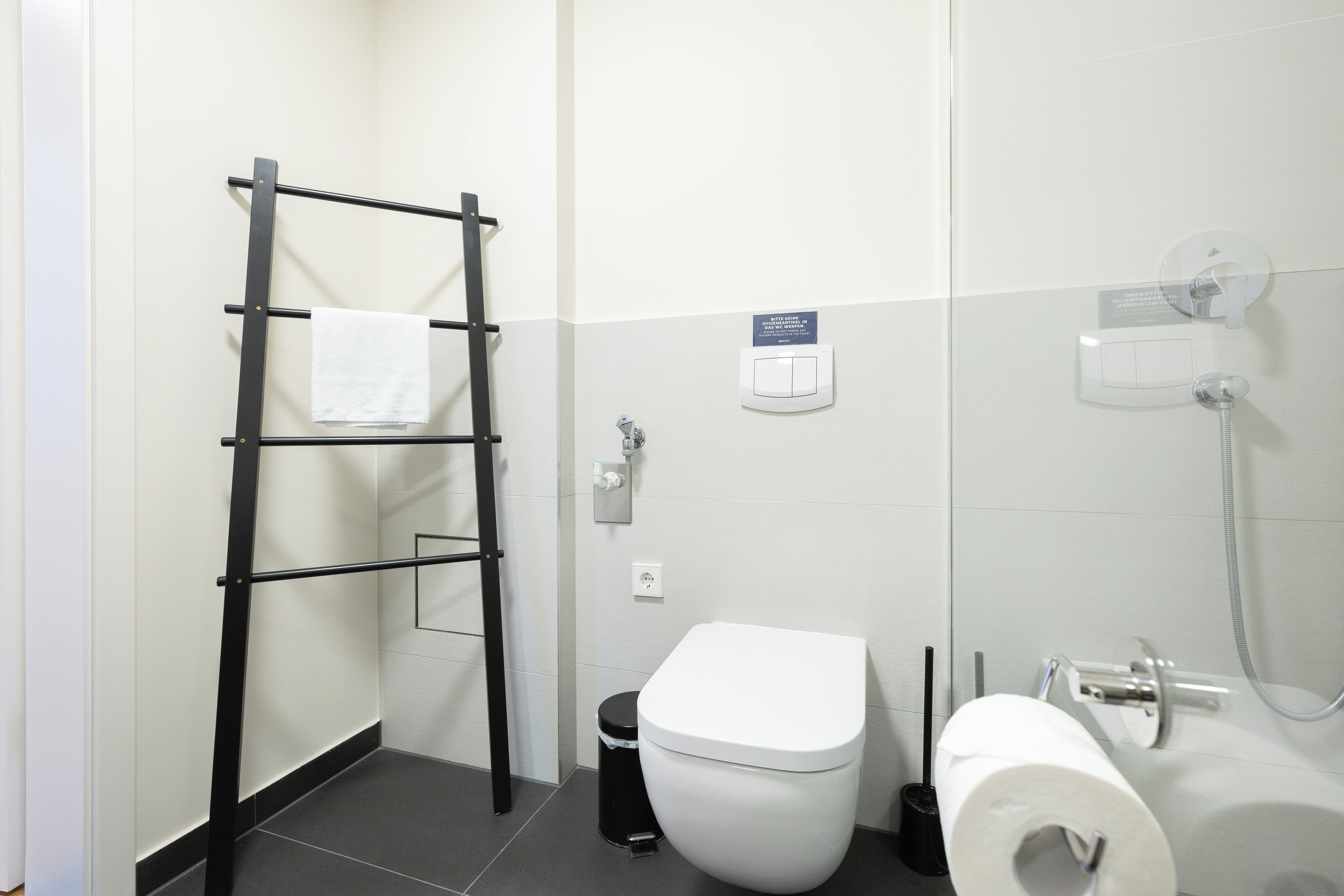 Een badkamer met een wit toilet, een zwarte handdoekhouder, een afvalbak en een douchegedeelte.