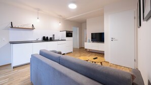 A modern apartment with a grey sofa, a small wooden table, a kitchen with white cabinets, and a TV on a white stand. - BRIGHT Leipzig Zentrum-West Stadium (Leipzig)