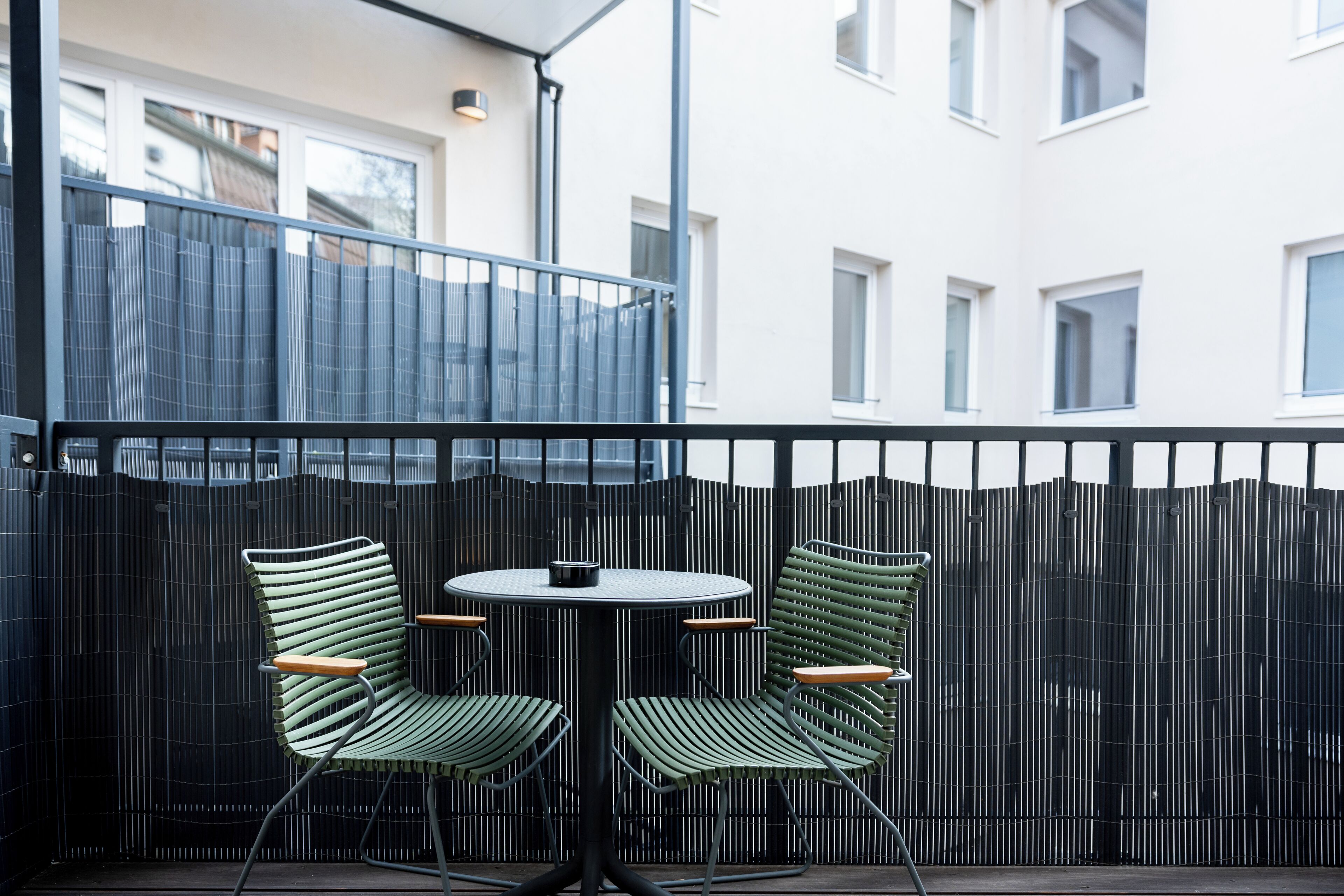A balcony with two green striped chairs and a small round table, enclosed by a black metal fence.