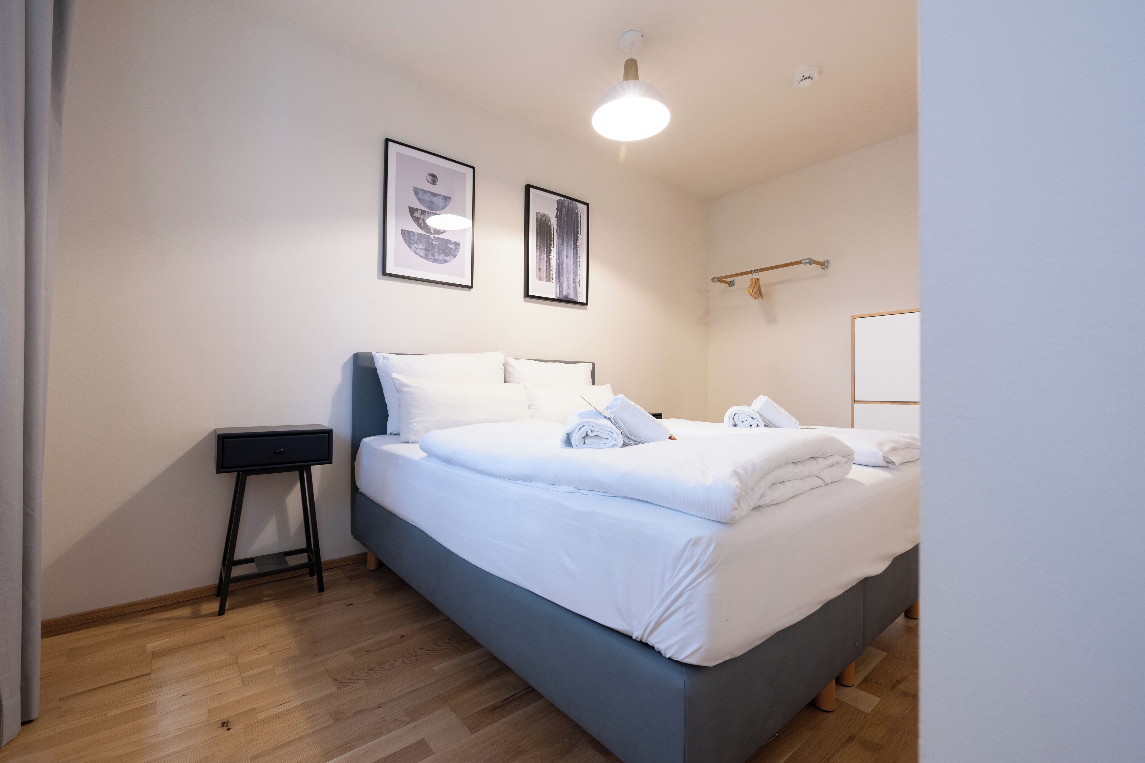 Een slaapkamer met een bed, een nachtkastje en twee ingelijste foto’s aan de muur.