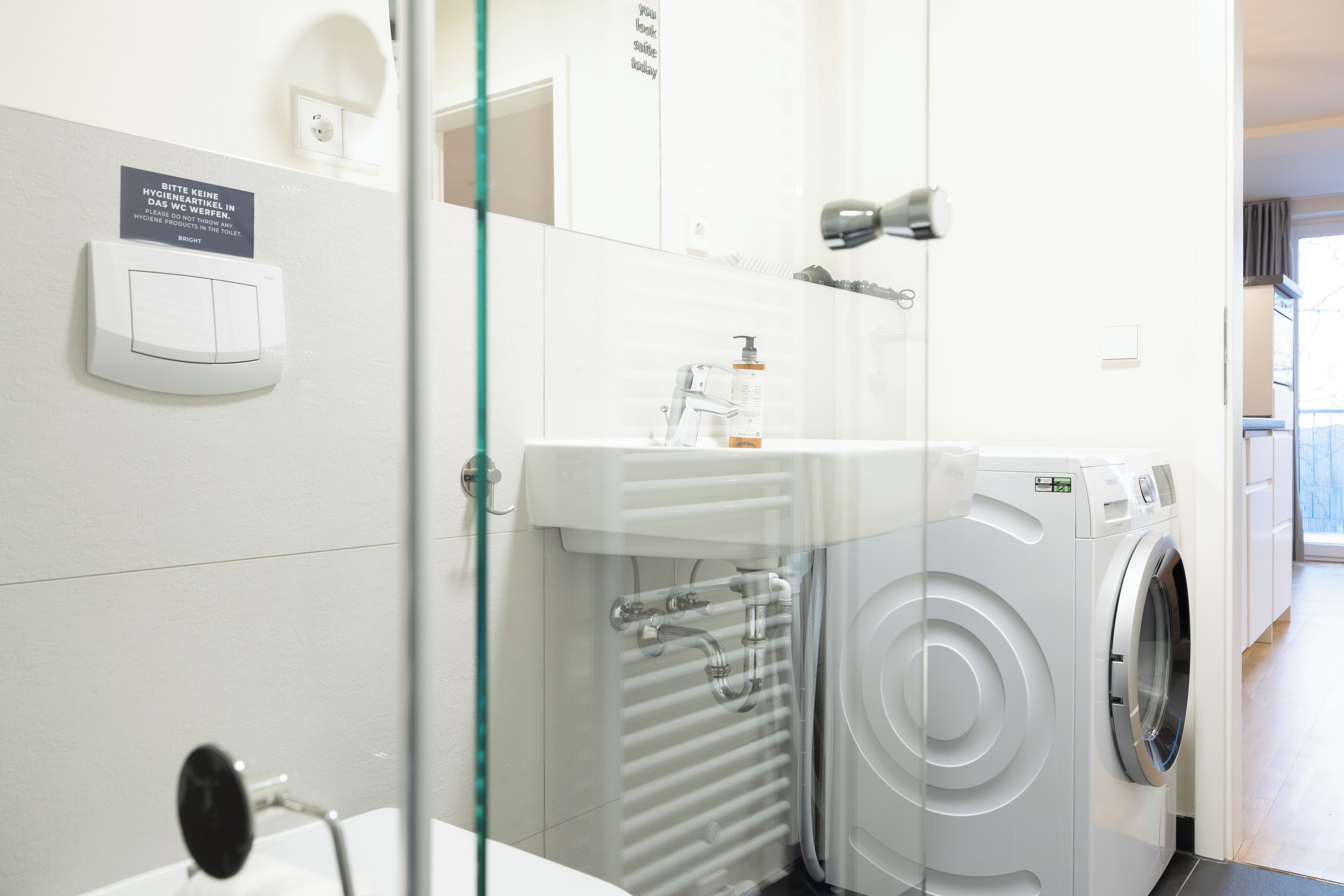 A modern bathroom with a washing machine, a sink, and a mirror.