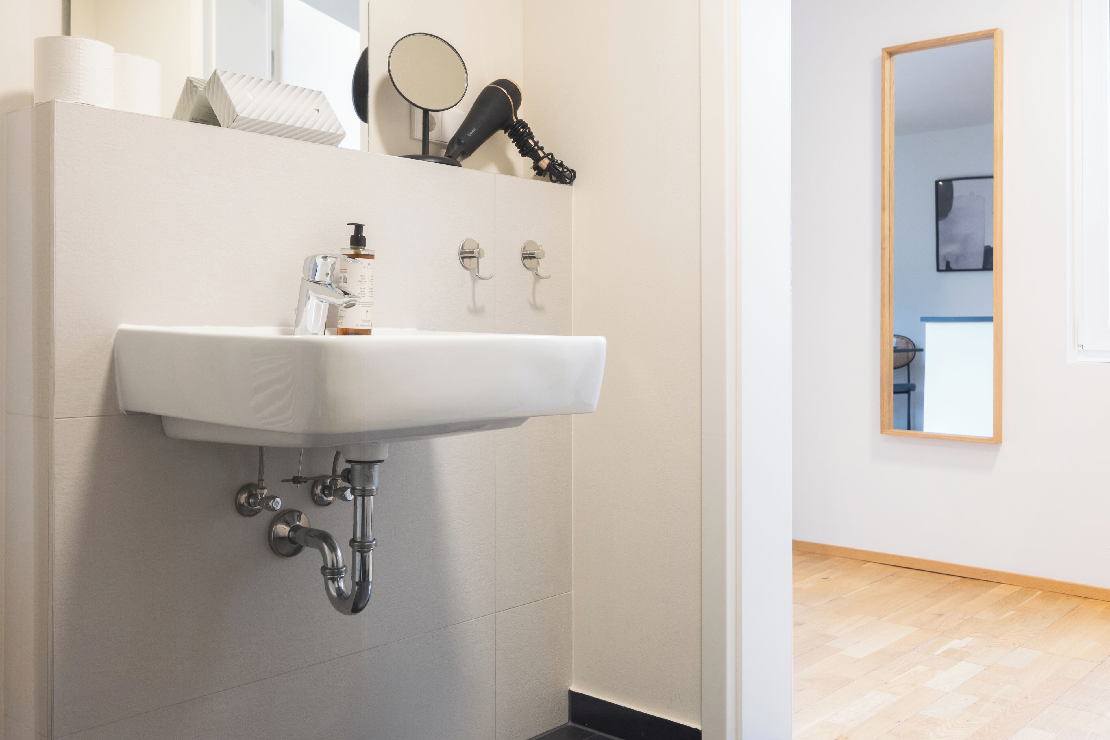A modern bathroom with a white sink, mirror, and hairdryer on a shelf.