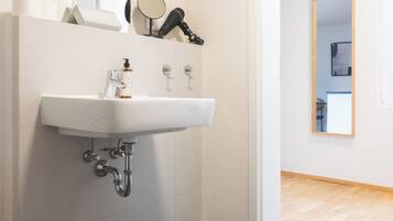 Un baño moderno con un lavabo blanco, espejo y secador de pelo en un estante.