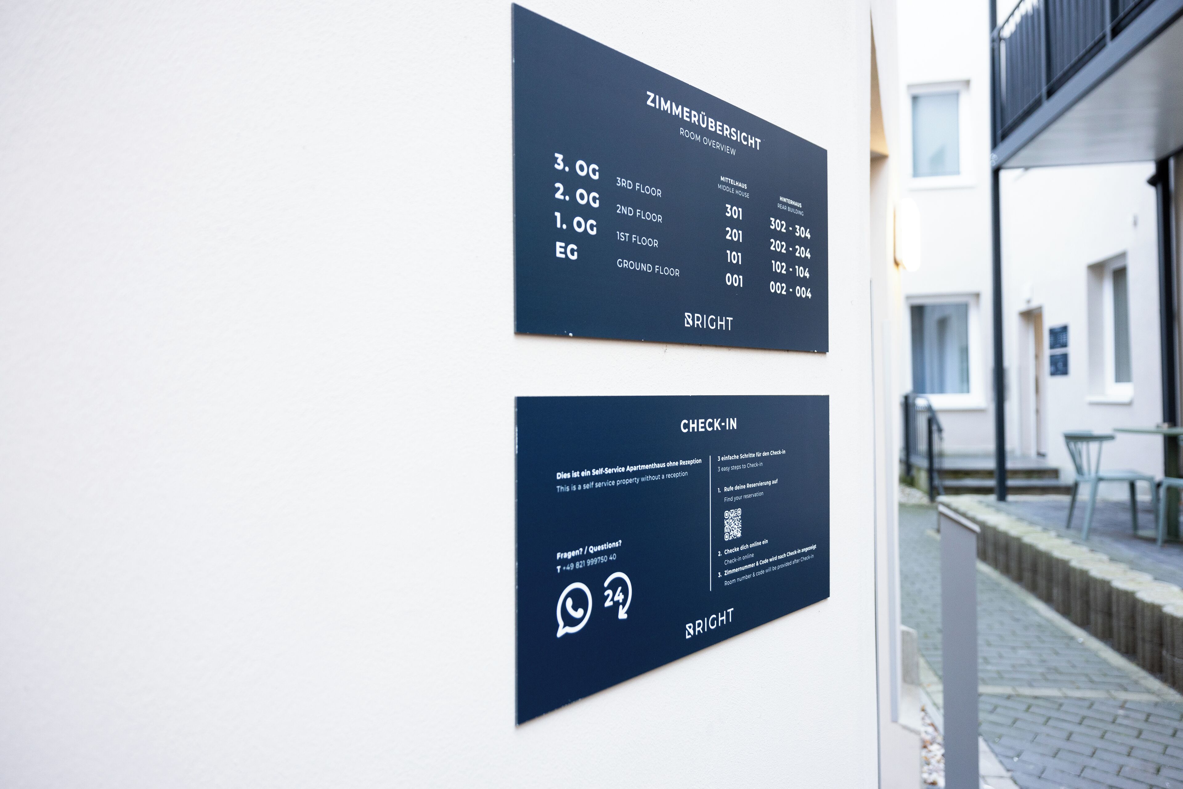 Two signs on a wall: one listing room numbers and floors, and another providing check-in information and a QR code for a self-service apartment reception.