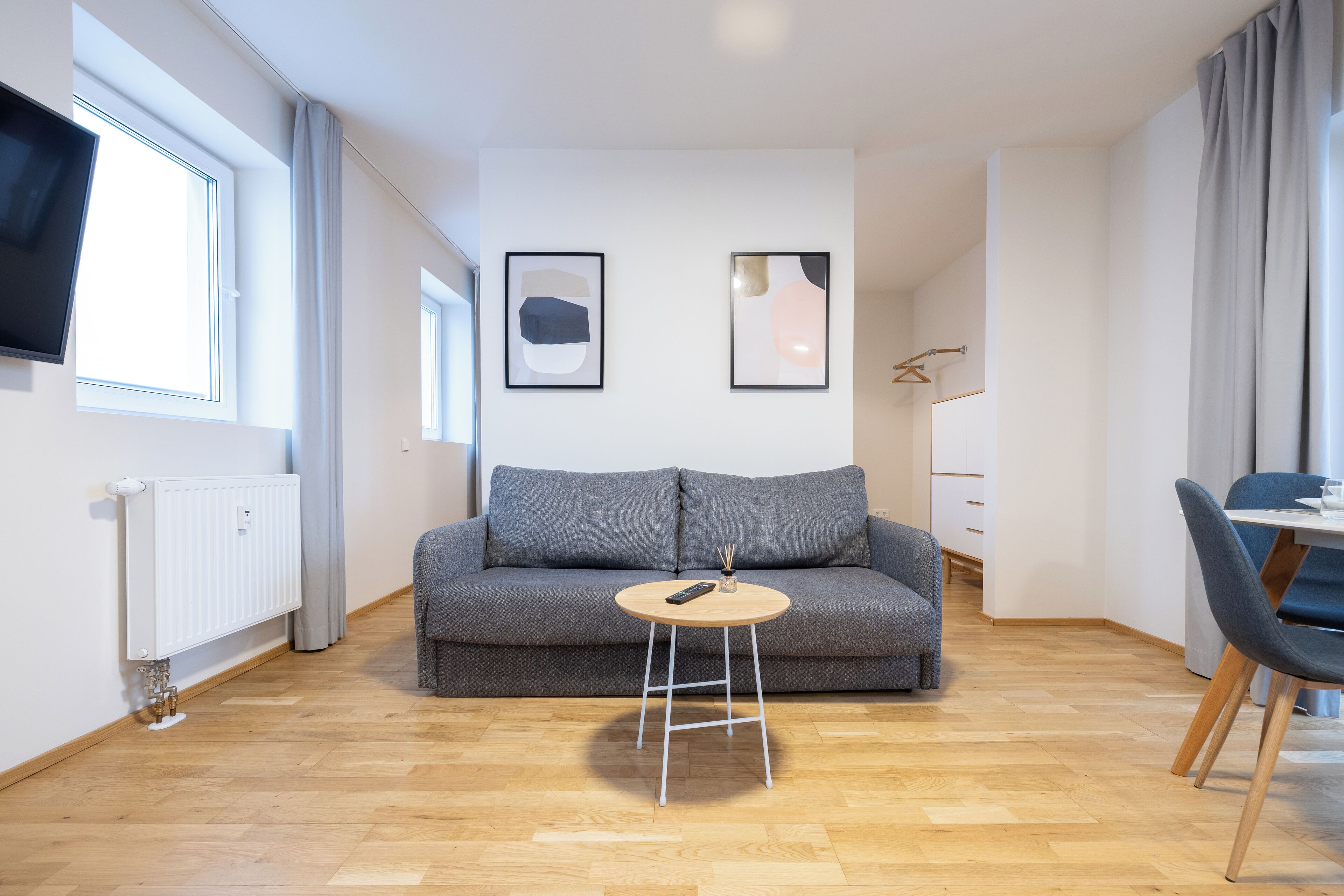 A modern living room with a grey sofa, a round wooden coffee table, and a flat-screen TV mounted on the wall.