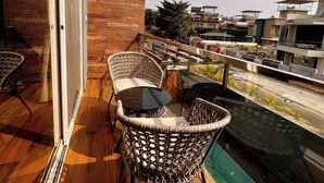 Un balcon agrémenté de fauteuils en osier et d’une table en verre, offrant une vue sur un paysage urbain avec des bâtiments modernes.