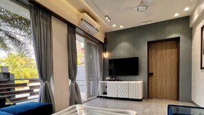 Un salon moderne avec une table basse en verre, des canapés bleus, un téléviseur à écran plat et une grande fenêtre avec des rideaux.