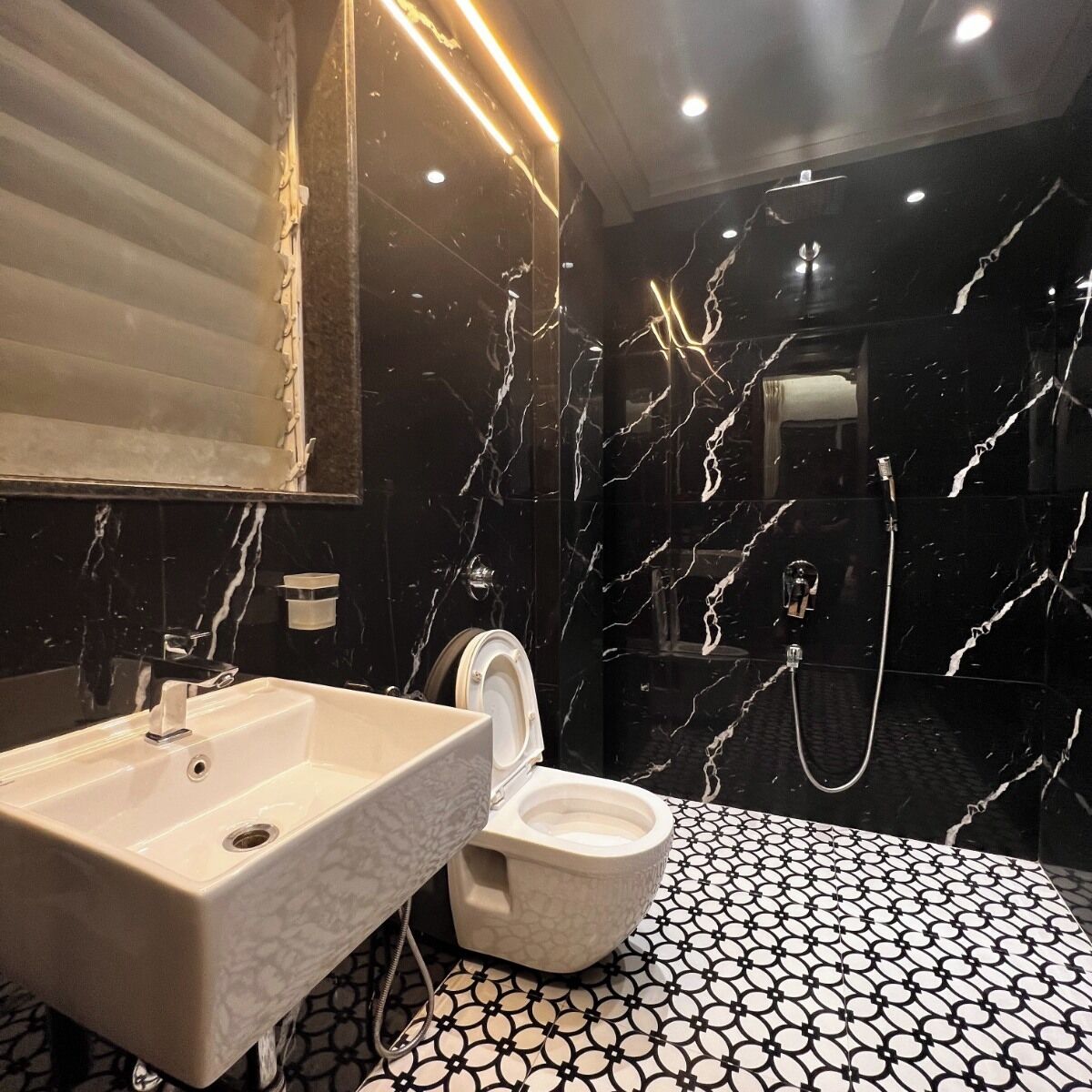Baño con lavamanos blanco, inodoro y ducha. El piso tiene un diseño de baldosas blanco y negro.