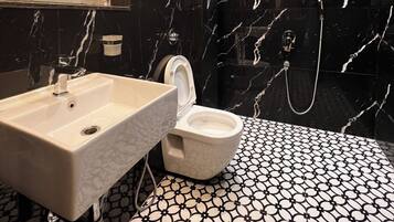 Baño con lavamanos blanco, inodoro y ducha. El piso tiene un diseño de baldosas blanco y negro.
