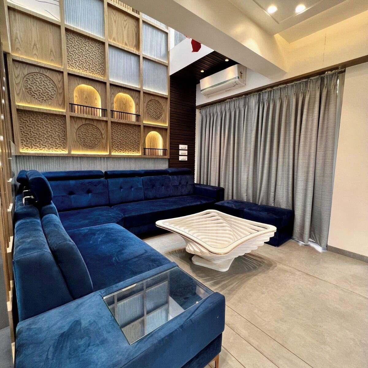 A modern living room with a blue sectional sofa, a glass coffee table, and a decorative wall panel.