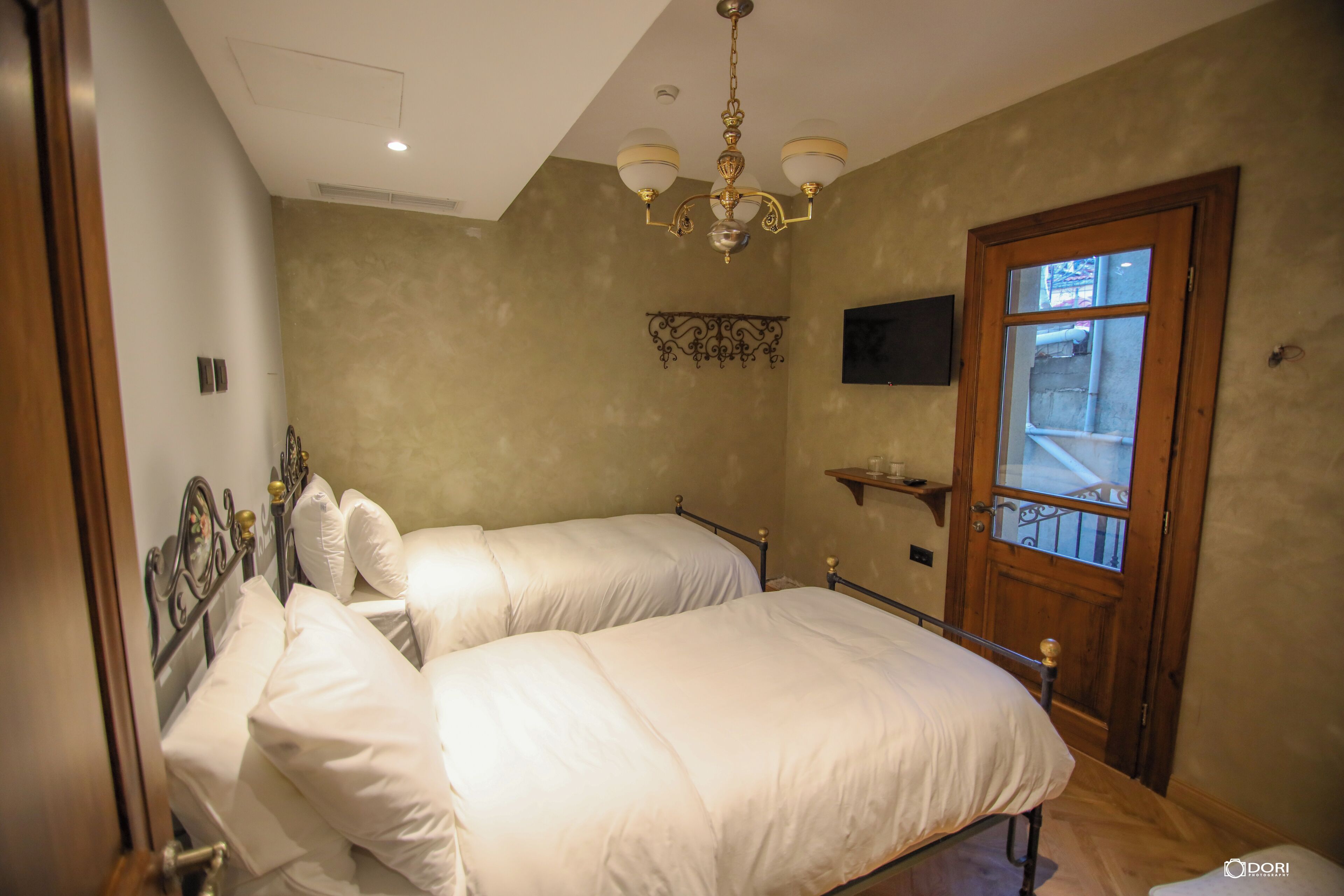 A bedroom with two beds, a chandelier, a television, and a window with a view.