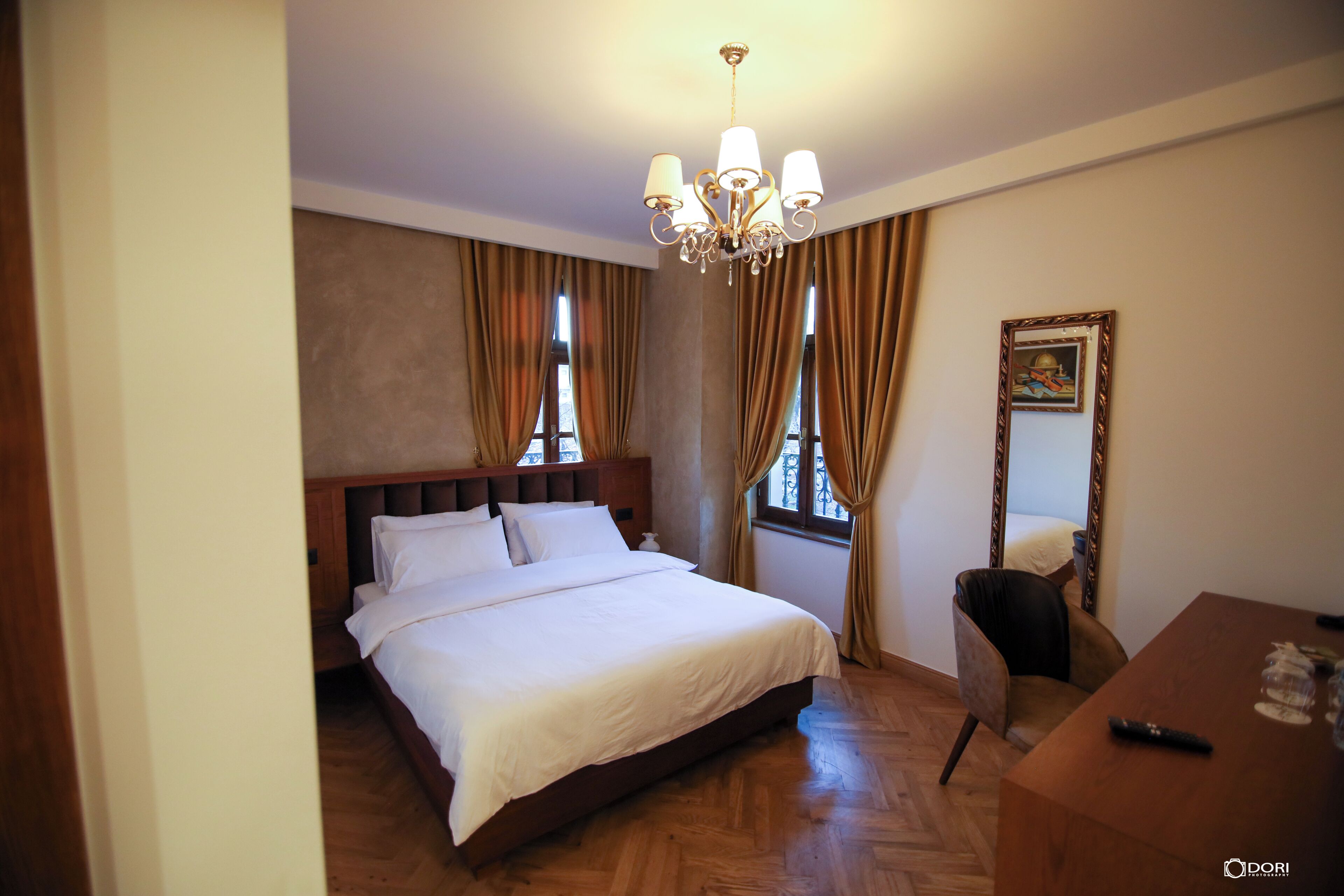 A hotel room with a large bed, a wooden headboard, a chandelier, a dining table, and a chair.